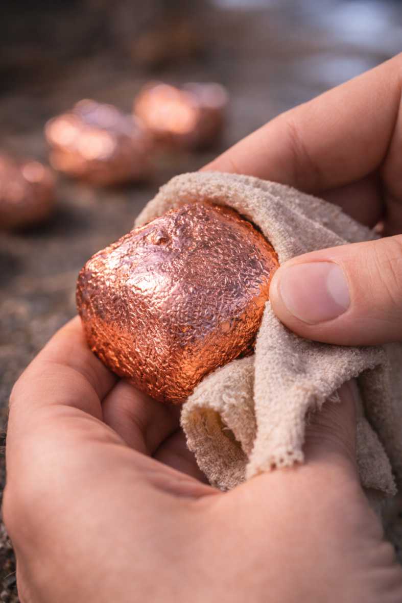 A hand polishing a copper plated Wombat Nugget